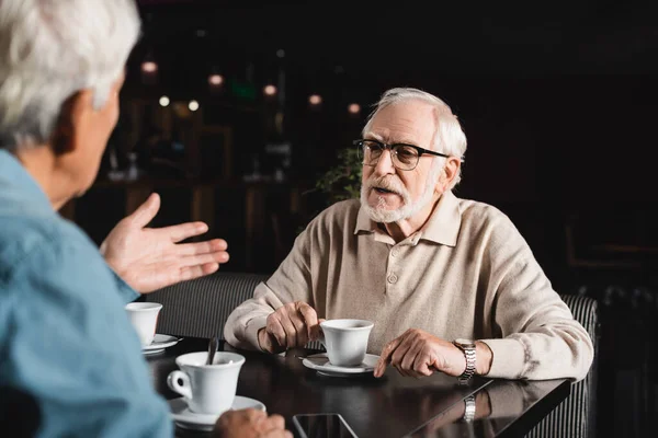 Blurred man pointing with hand while talking to senior friend in cafe — Stock Photo