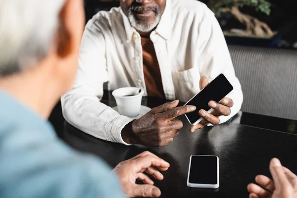 Partial view of senior african american man pointing at smartphone with blank screen near blurred friend — Stock Photo