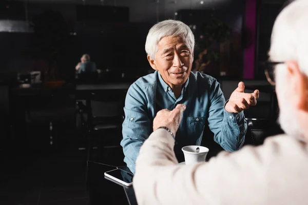 Senior asiatique homme et son flou ami gestuelle pendant conversation dans café — Photo de stock