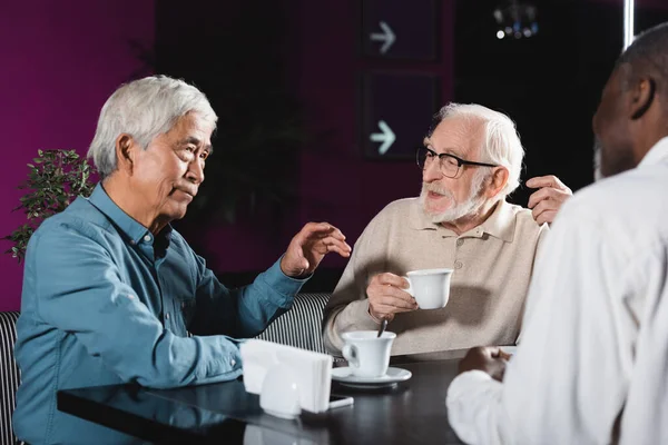 Elderly multiethnic friends drinking coffee and talking in cafe — Stock Photo