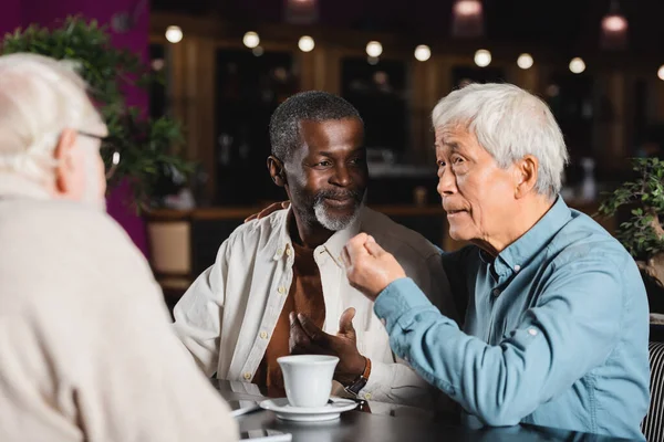Senior asian man gesturing while talking to multicultural friends in restaurant — Stock Photo