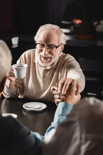 Alegre hombre mayor uniendo las manos con borrosa interracial amigos en la cafetería - foto de stock