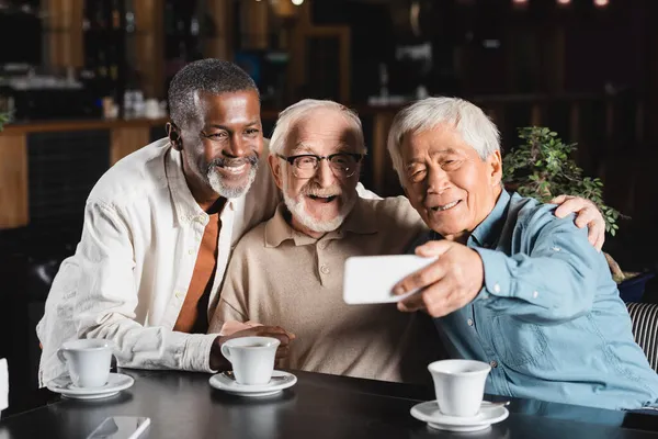 Anziano asiatico uomo presa selfie con felice multietnico amici in ristorante — Foto stock