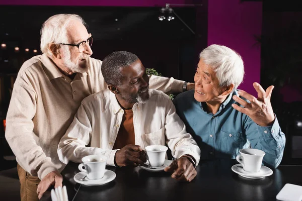 Emocional asiático hombre gesto mientras habla a alegre multicultural amigos en café — Stock Photo
