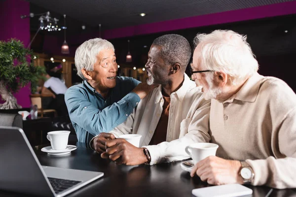 Eccitato asiatico uomo toccare spalla di anziano africano americano amico in caffè — Foto stock