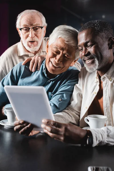 Fröhliche multiethnische Senioren, die im Café auf ihr digitales Tablet schauen — Stockfoto