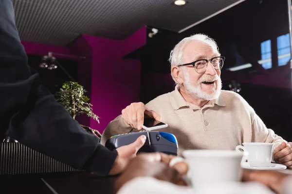 Senior en lunettes payer avec smartphone via terminal de paiement dans pub — Photo de stock