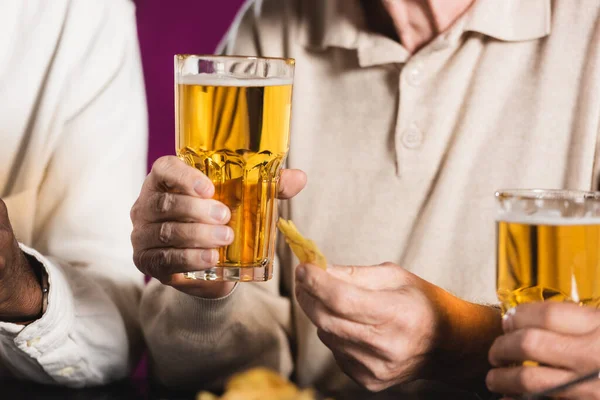 Vista recortada del hombre mayor sosteniendo un vaso de cerveza y patatas fritas cerca de amigos en el pub - foto de stock