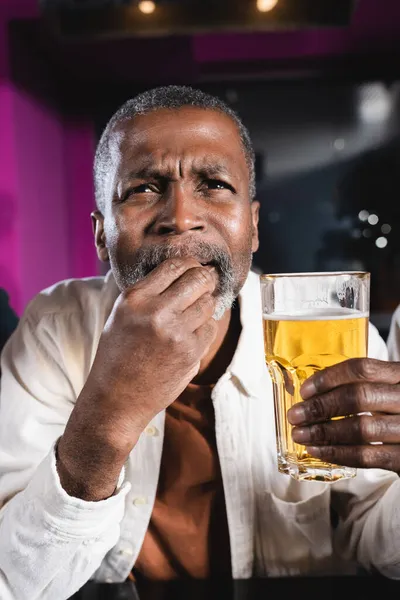 Homem americano africano sênior segurando copo de cerveja enquanto assiste campeonato no bar de esportes — Fotografia de Stock