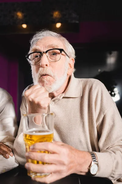 Homme âgé tendu avec poing serré et verre de bière regarder match de football dans le bar sportif — Photo de stock