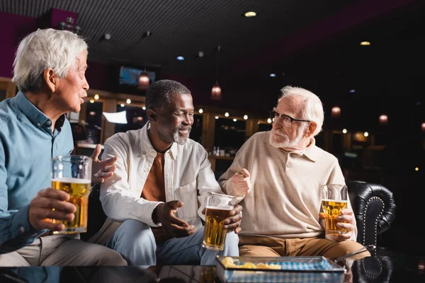 Amigos multiculturales de alto nivel haciendo gestos mientras hablan en el pub de cerveza - foto de stock