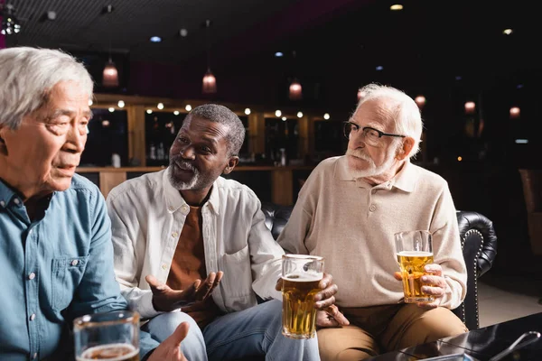 Africano americano hombre gesto durante conversación con senior interracial amigos en pub - foto de stock