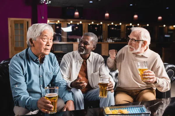Senior interracial friends gesturing while talking to asian friend in pub — Stock Photo