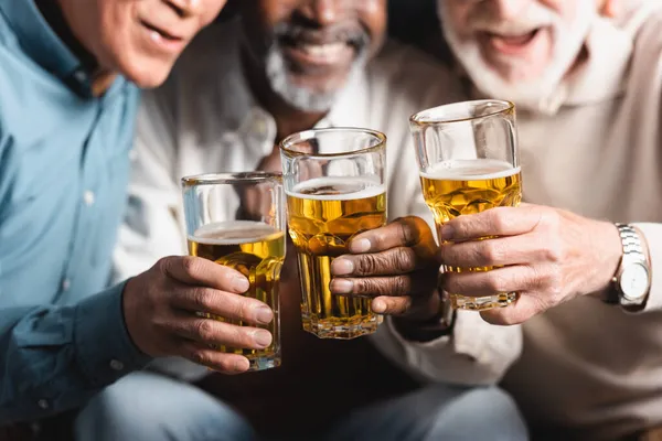 Recortado vista de borrosa multiétnica amigos tintineo vasos de cerveza en pub - foto de stock