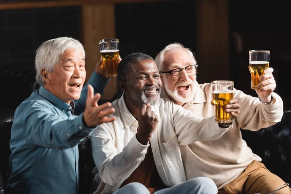 Senior african american man showing triumph gesture near excited multiethnic friends watching football in sports bar — Stock Photo