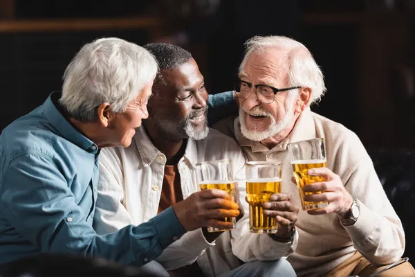 Amici multietnici felici e anziani che tengono bicchieri di birra mentre trascorrono del tempo al pub — Foto stock