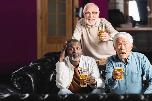 Emocionado seniores amigos multiculturais com copos de cerveja assistindo jogo de futebol no bar de esportes — Fotografia de Stock