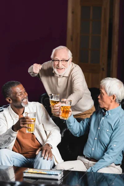 Feliz hombre mayor mostrando gesto de victoria mientras ve el campeonato de fútbol con amigos interracial - foto de stock