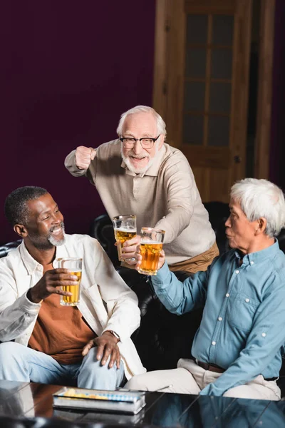 Heureux senior montrant geste de victoire tout en regardant le championnat de football avec des amis interraciaux — Photo de stock