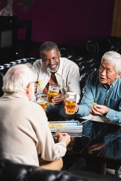 Старші та позитивні багатоетнічні друзі розмовляють під час пиття пива та їжі чіпсів у барі — стокове фото
