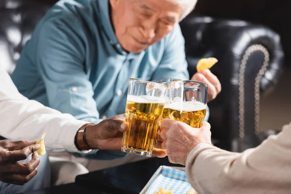 Blurred asian man clinking beer glasses with multicultural friends in pub — Stock Photo