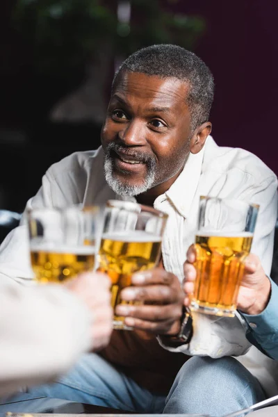 Senior homme afro-américain souriant tout en cliquetis flous verres à bière avec des amis — Photo de stock