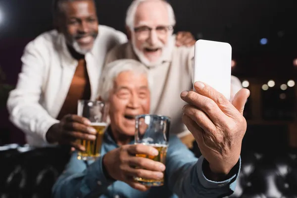 Blurred asian man taking selfie on mobile phone with senior friends in beer pub — Stock Photo