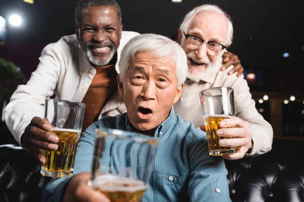 Fröhliche Senioren-Multikulti-Freunde blicken in die Kamera, während sie in der Kneipe Biergläser halten — Stockfoto