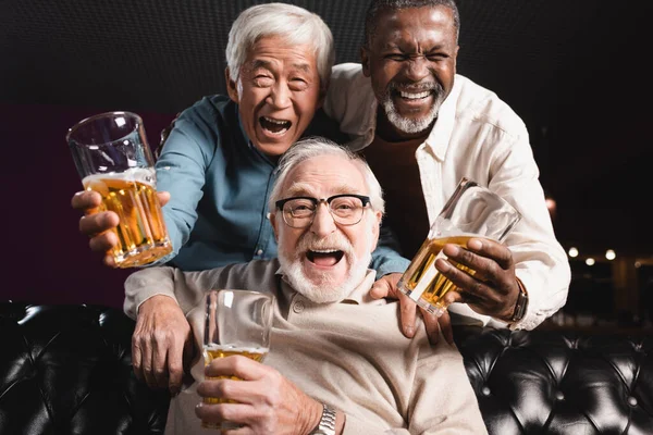 Elderly friends with glasses of beer laughing at camera in pub — Stock Photo