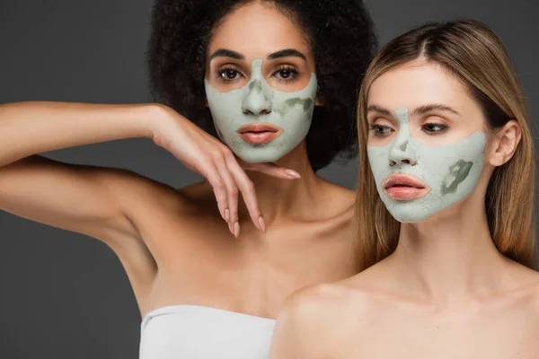 African american woman in clay mask looking at camera near friend isolated on grey — Stock Photo