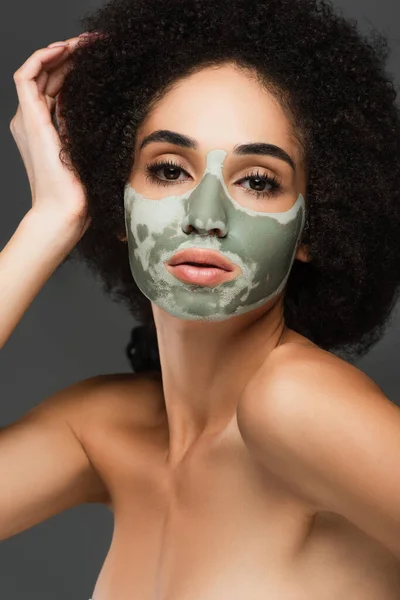 Sensuale donna afroamericana con spalle nude e maschera di argilla sul viso guardando la fotocamera isolata sul grigio — Foto stock