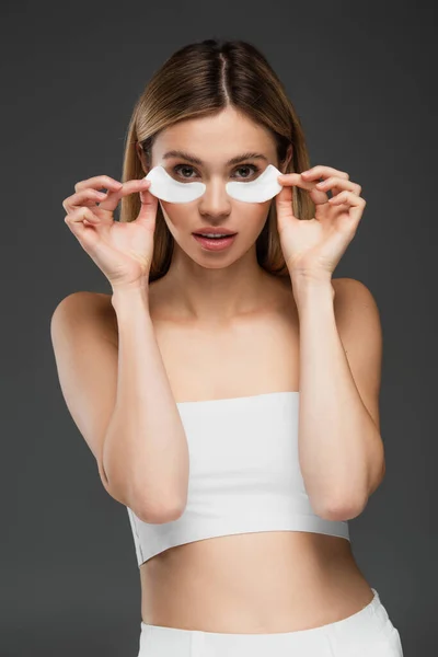 Hübsche Frau in weißem Top mit Kollagen-Augenklappen isoliert auf grau — Stockfoto
