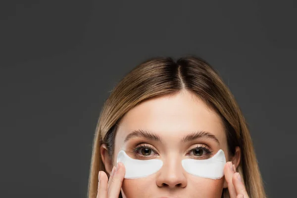 Partial view of woman applying collagen eye patches isolated on grey — Stock Photo