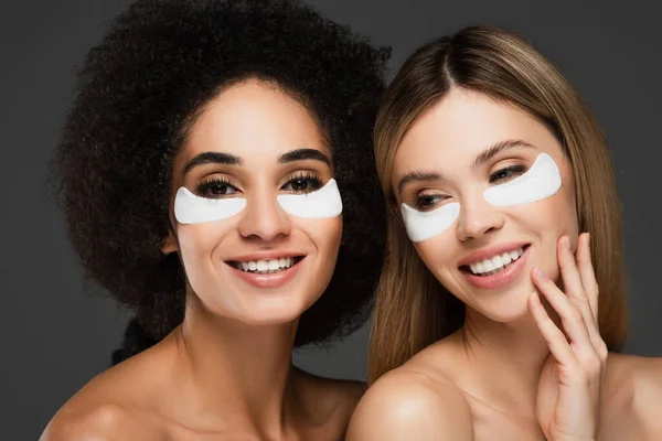 Mujeres bastante multiétnicas en parches de colágeno sonriendo aisladas en gris - foto de stock