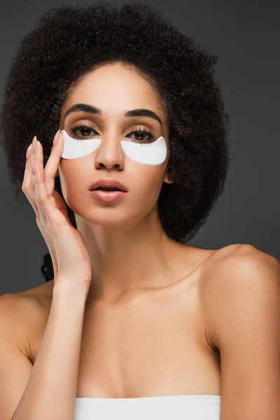 Afro-américaine avec épaules nues touchant bandeau oculaire sur le visage isolé sur gris — Photo de stock