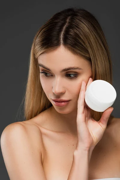 Bella donna con spalle nude tenendo crema cosmetica isolata su grigio — Foto stock