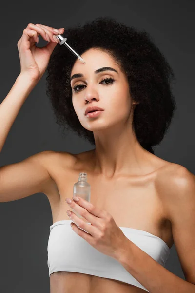 Young african american woman applying cosmetic serum on forehead isolated on grey — Stock Photo
