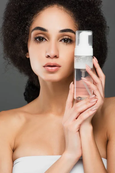 Junge afrikanisch-amerikanische Frau mit perfekter Haut und natürlichem Make-up hält Reinigungsschaum isoliert auf grau — Stockfoto