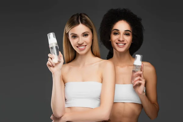 Hübsche interrassische Frauen mit perfekter Haut und natürlichem Make-up posieren mit Reinigungsschaum isoliert auf grau — Stockfoto