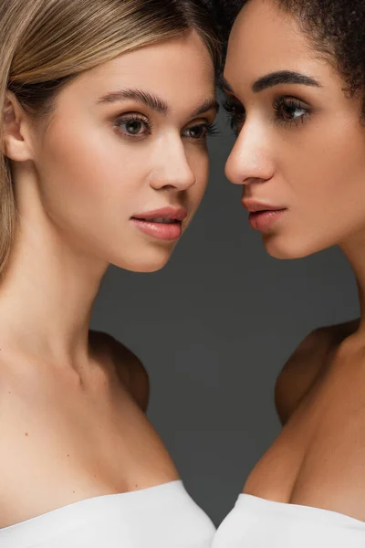 Крупный план молодых многоэтнических женщин с идеальной кожей и естественным макияжем, изолированных от серого — стоковое фото