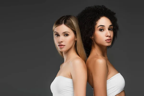 Pretty interracial women with perfect skin looking at camera isolated on grey — Stock Photo