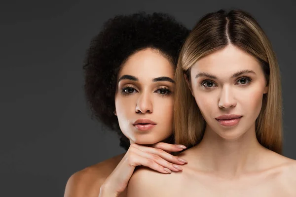 Mujeres jóvenes y bastante multiétnicas con la piel perfecta y maquillaje natural mirando a la cámara aislada en gris - foto de stock