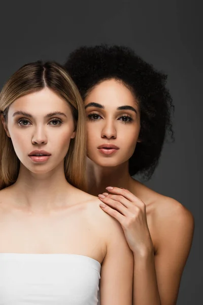 Sensual multiethnic women with perfect skin and naked shoulders looking at camera isolated on grey — Stock Photo