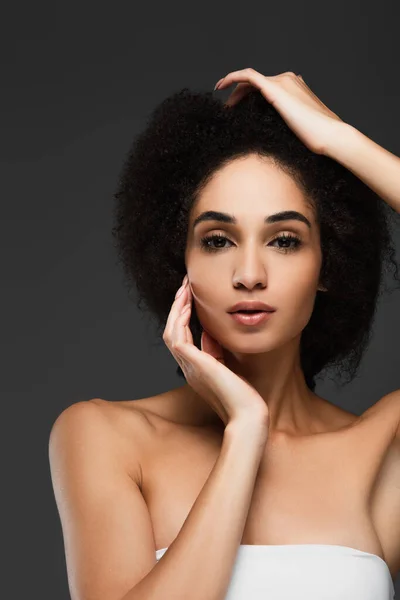 Sensual mujer afroamericana con la piel perfecta y hombros desnudos mirando a la cámara aislada en gris - foto de stock