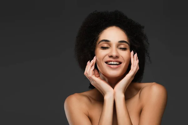 Щаслива афроамериканська жінка з закритими очима торкається досконалої шкіри на обличчі ізольована на сірому — стокове фото