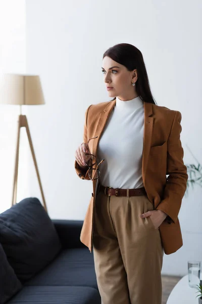 Psicólogo sosteniendo gafas y mirando hacia otro lado mientras está de pie con la mano en el bolsillo — Stock Photo