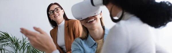 Psychologist in eyeglasses smiling near interracial lesbian couple gaming in vr headsets, banner — Stock Photo