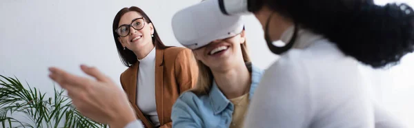 Psychologue dans les lunettes souriant près interracial lesbienne couple gaming dans vr headsets, bannière — Photo de stock