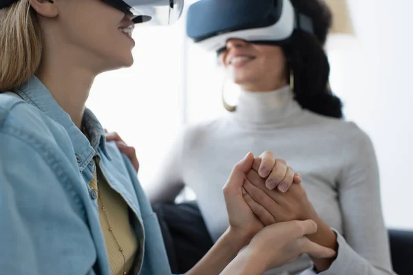 Happy same sex couple holding hands while gaming in vr headsets, blurred background — Stock Photo