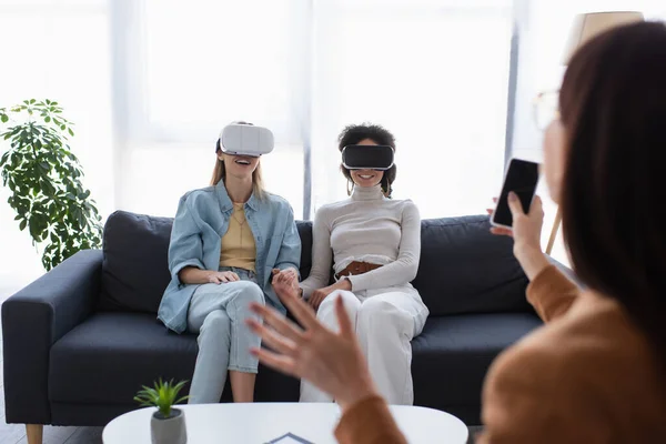 Psicólogo desfocado com telefone celular perto de mulheres lésbicas inter-raciais em fones de ouvido vr — Fotografia de Stock